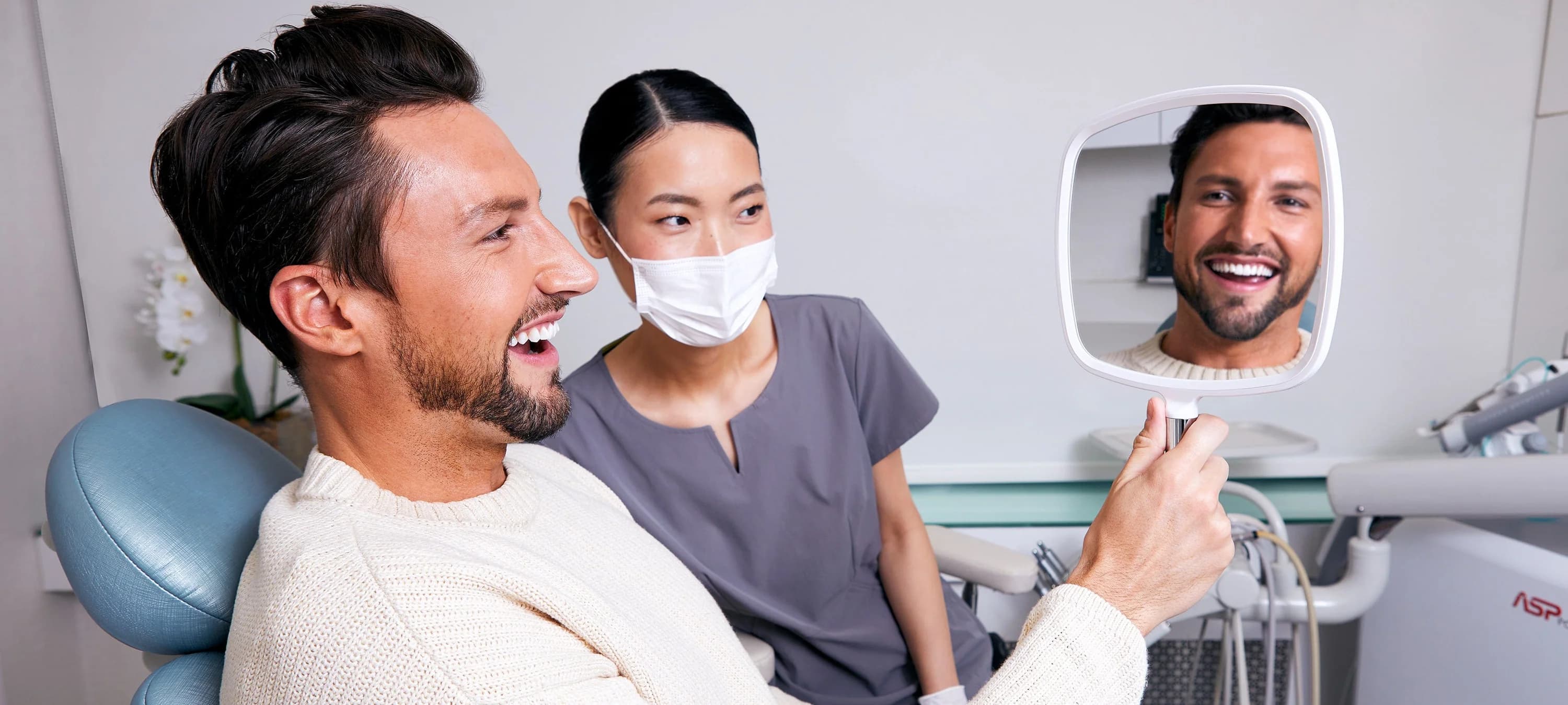 Patient admiring his brighter smile in a hand mirror with a Miller Dental Care team member