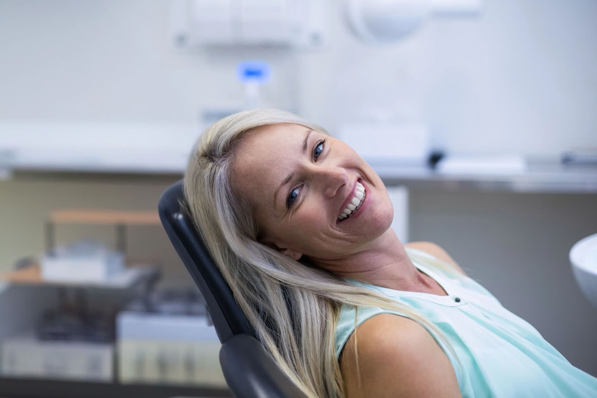 A dental patient smiles while checking her teeth in a mirror during a cosmetic consultation.