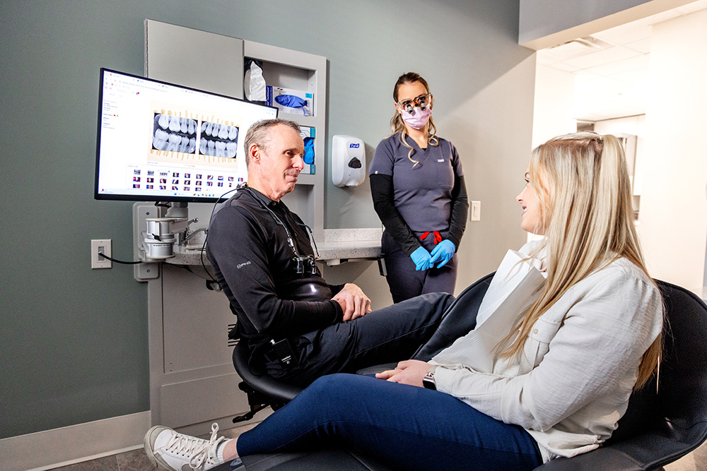 Dentist reviewing dental X-rays with a female patient seated in a dental chair while a dental assistant stands nearby in a modern dental clinic.Dentist reviewing dental X-rays with a female patient seated in a dental chair while a dental assistant stands nearby in a modern dental clinic.